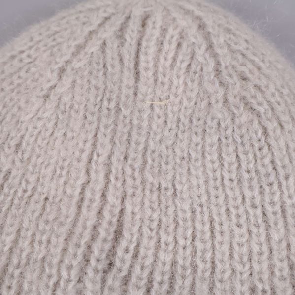 Närbild på garnstruktur av beige stickad mössa