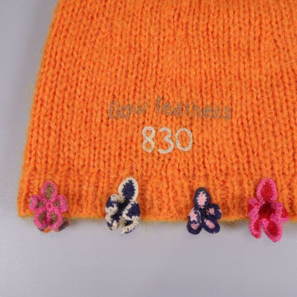 Detaljbild på blommor längs kanten på orange mössa
