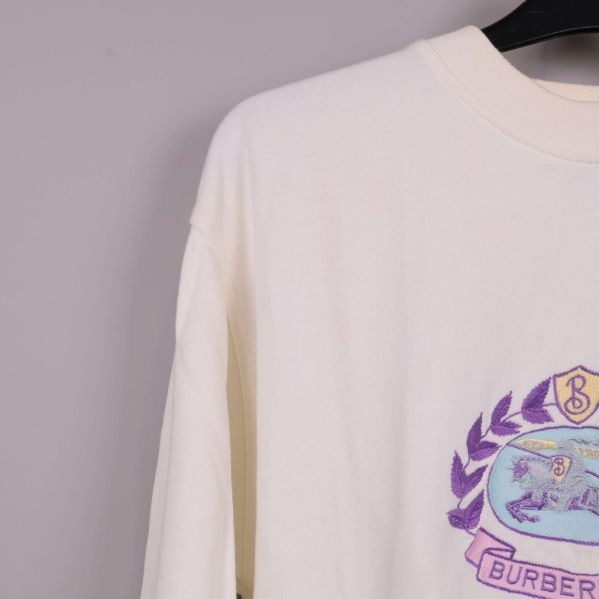 Axel och överdel av gräddvit sweatshirt med broderad logga syns