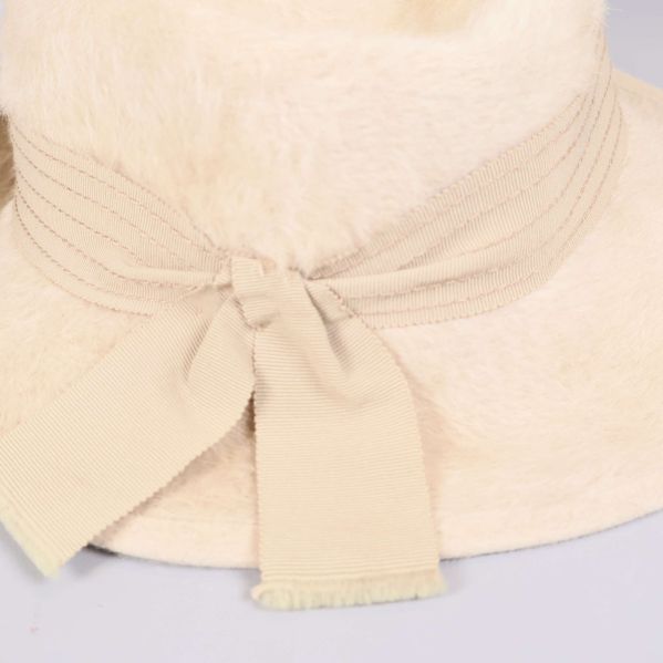 Närbild på krämvit rosett och sydd hattkant i textil