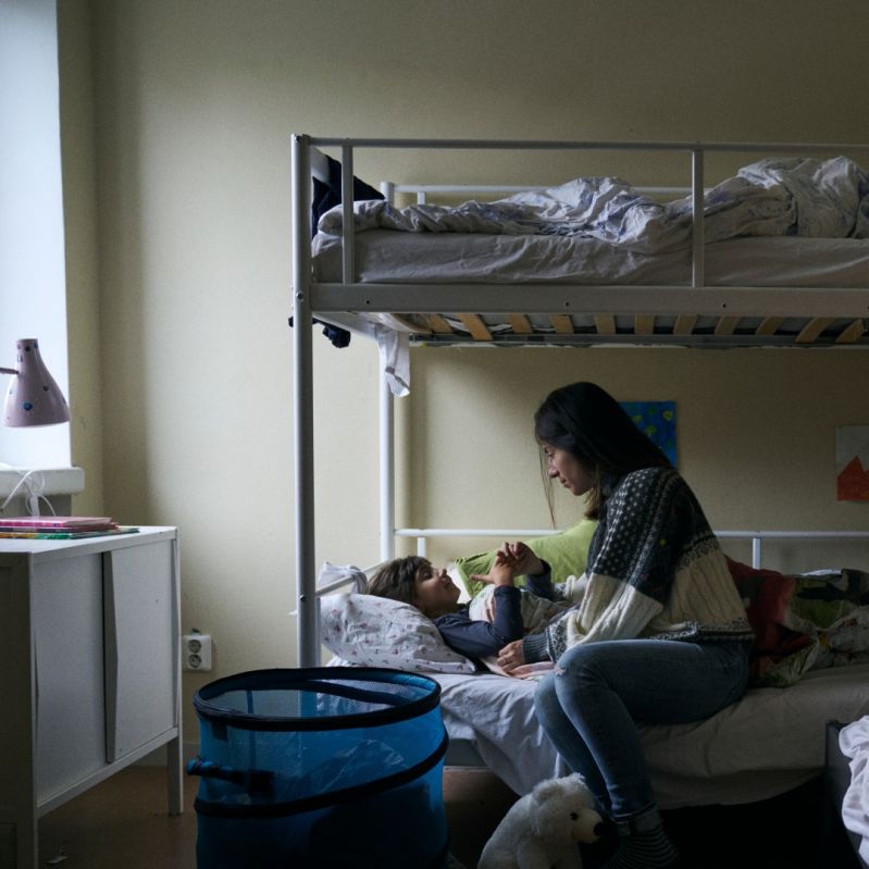 En flicka ligger i en våningssäng och en mamma sitter vid sängkanten. De samtalar. 