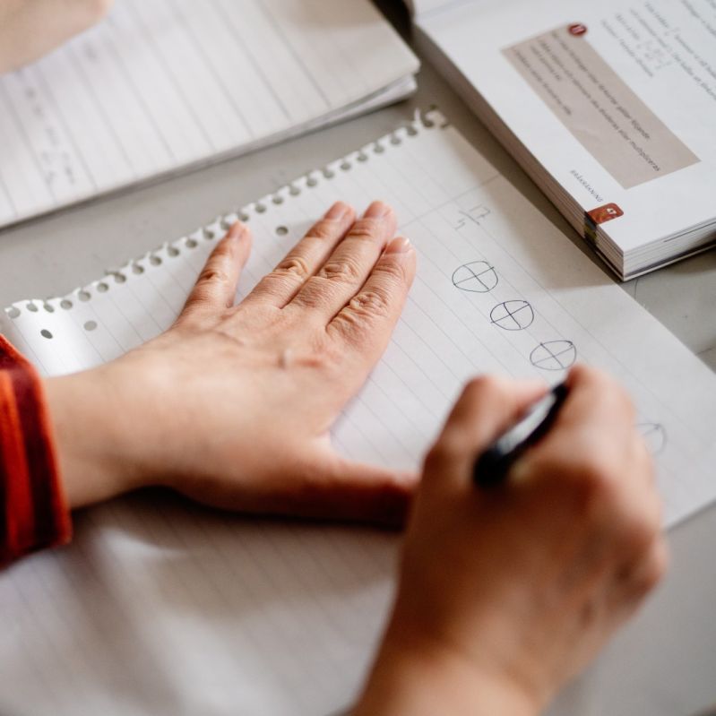 Bild person sitter och pluggar, man ser hander som skriver på ett papper.
