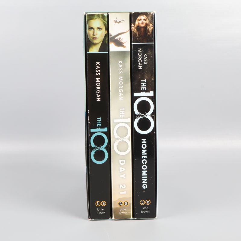 Tre böcker i boxen The 100 med ryggar synliga och porträtt av karaktärer