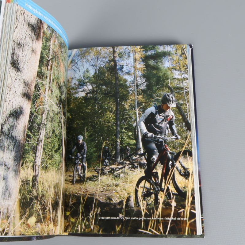 Uppslag med cyklister på stig i skog, från stigcyklingsbok