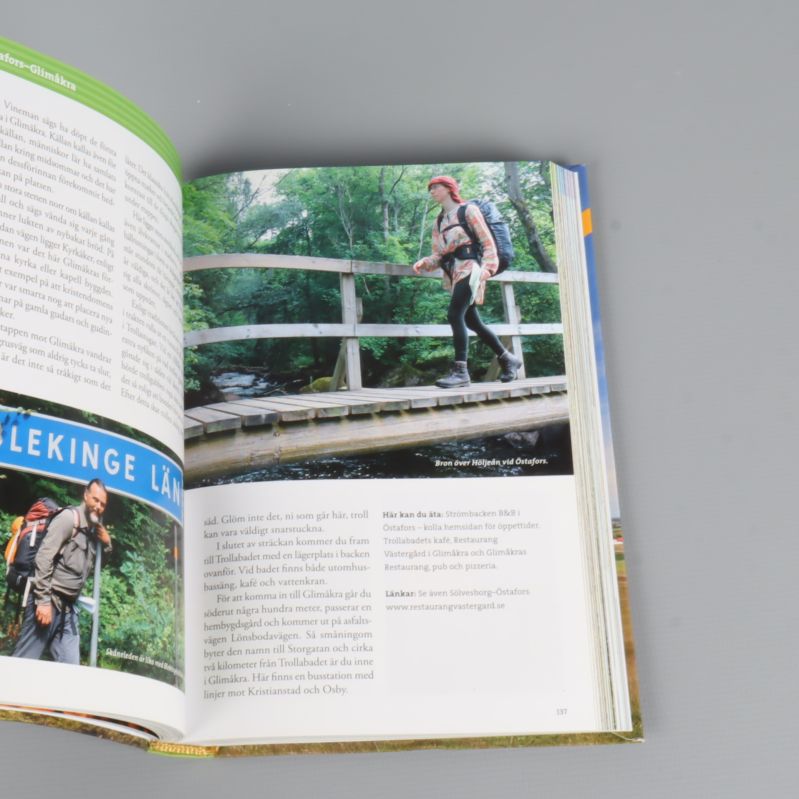 Uppslag med vandrare på bro och naturmiljö i guidebok