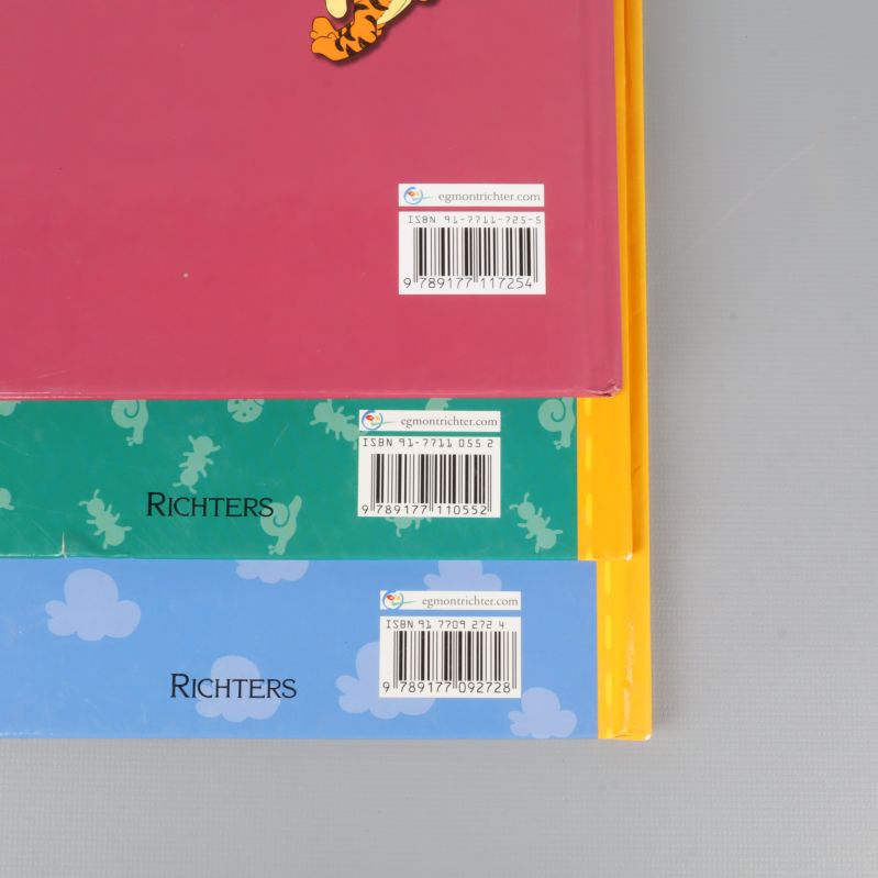 Närbild på tre baksidor av Nalle Puh-böcker med synliga ISBN