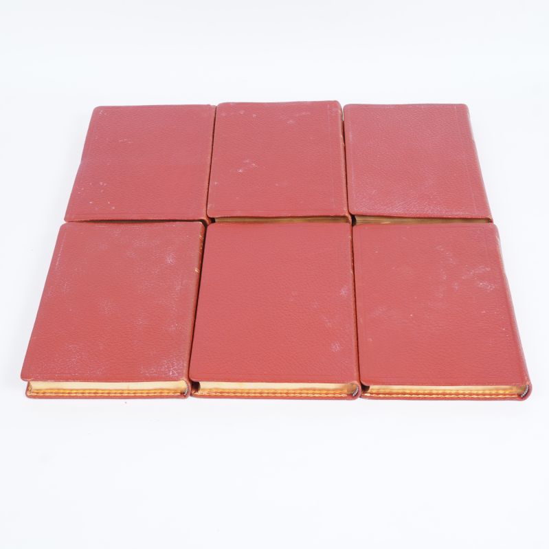 Sex röda böcker, liggande med baksidorna synliga och guldkantade sidor