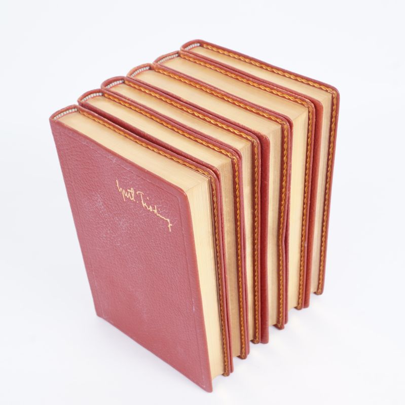 Sex stående röda böcker med gulddetaljer och sydda kanter