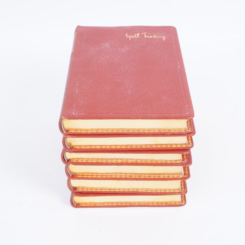 Staplade röda böcker med gulddetaljer och präglad signatur