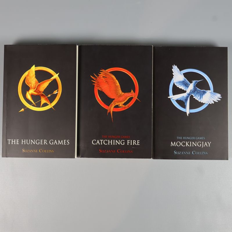 Tre framsidor av The Hunger Games-böcker, varje med egen symbol och färg