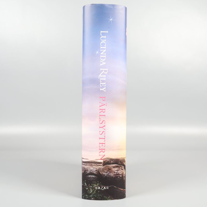 Bokrygg med titeln Pärlsystern och Lucinda Riley i vitt mot blå bakgrund