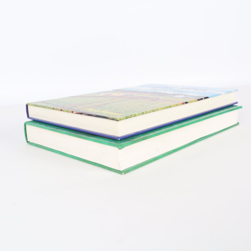 Två tjocka inbundna böcker lagda på varandra, sedd från sidan