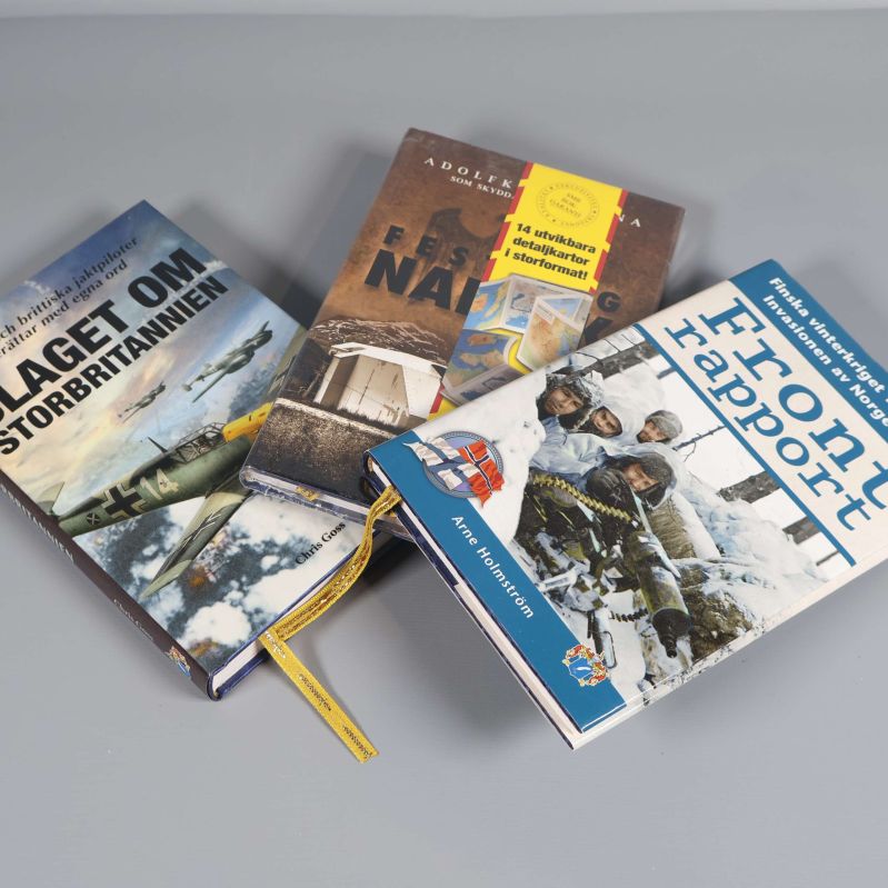Tre militärhistoriska böcker sedda snett uppifrån liggande på bord