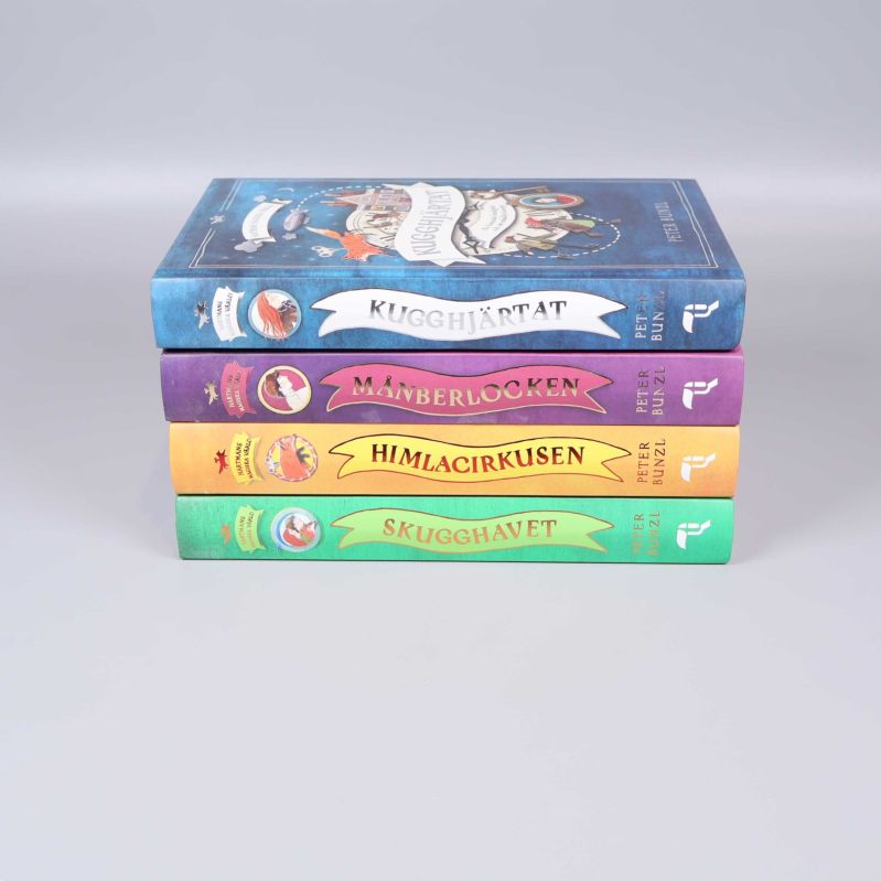 Ryggar på fyra staplade böcker med titlar och färger ur Hartmans magiska värld