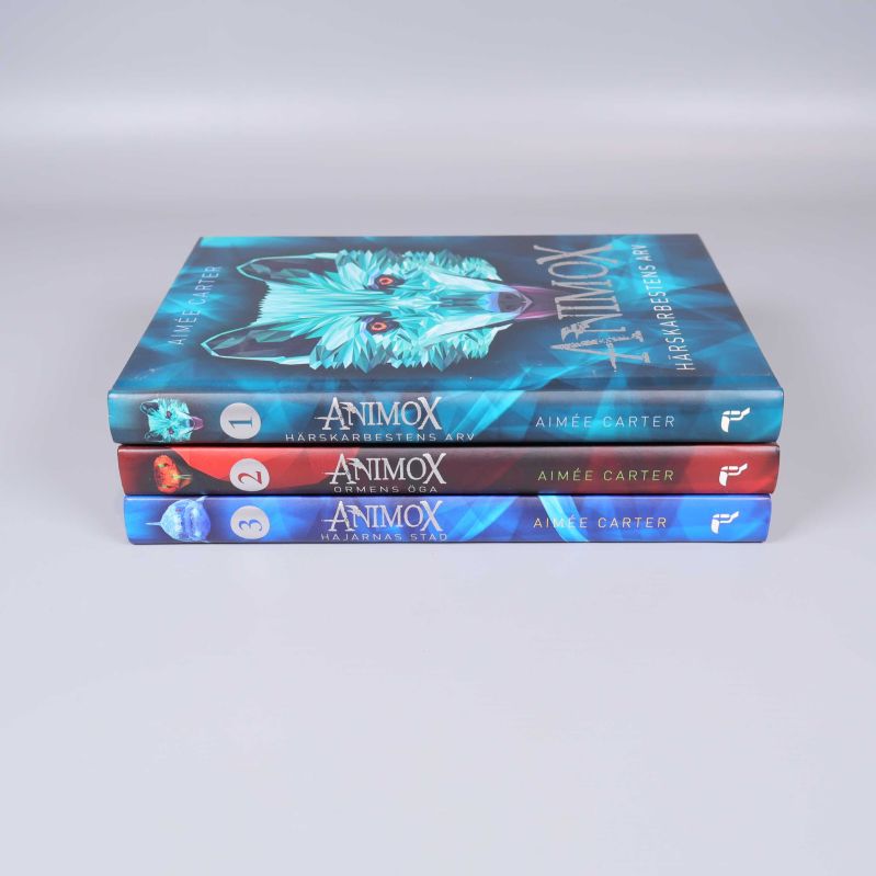 Tre staplade Animox-böcker med ryggar mot kameran