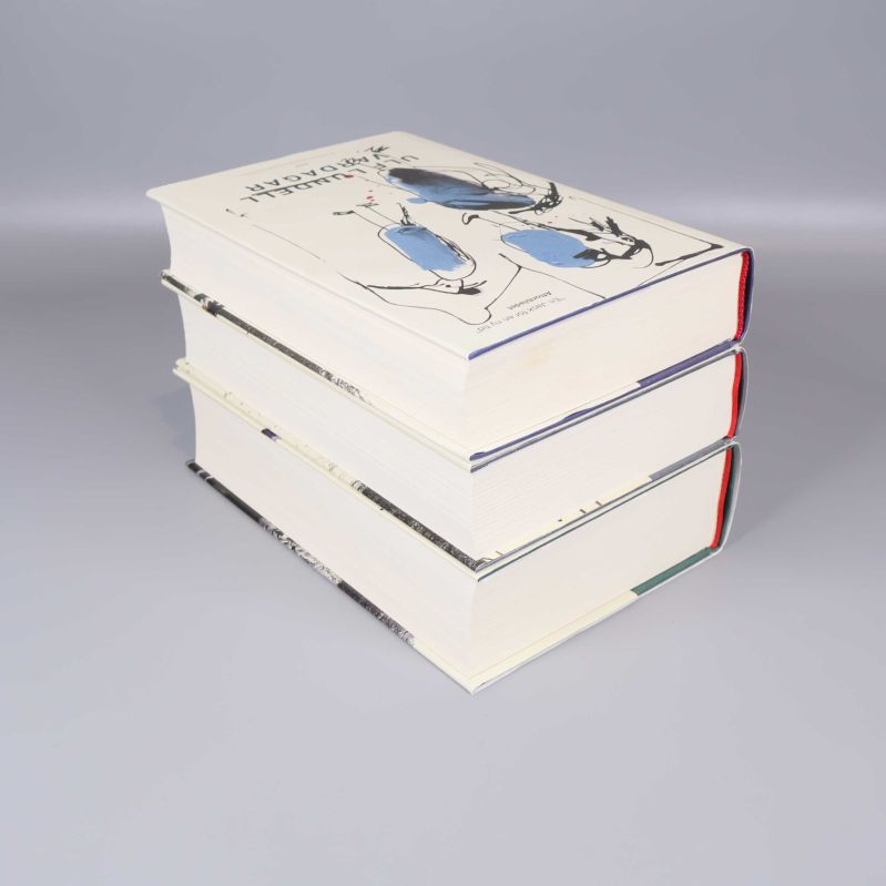 Tre tjocka böcker staplade snett, visar sidor och övre del av omslag