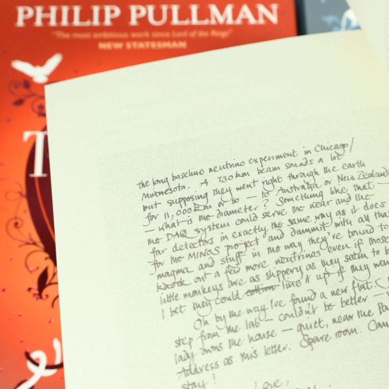 Närbild på handskriven sida inuti The Subtle Knife med bok i bakgrunden