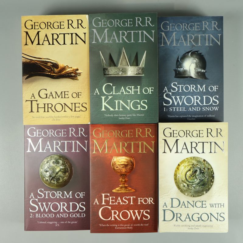 Framsidor av sju böcker i A Song of Ice and Fire liggande mot en ljus bakgrund