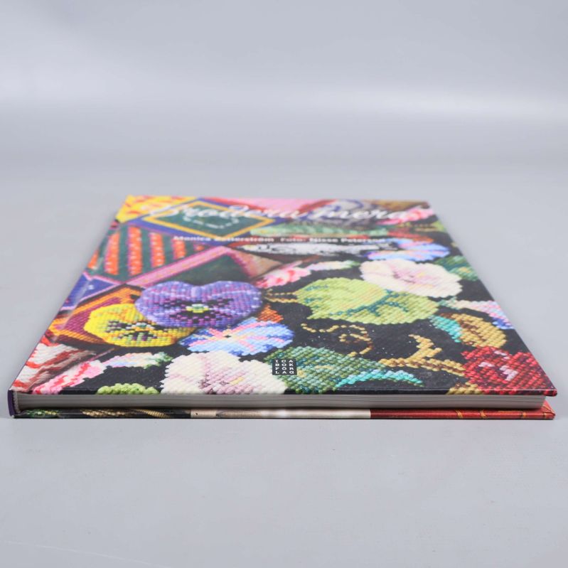 Boken Brodera mera liggande på ett bord, visad från sidan