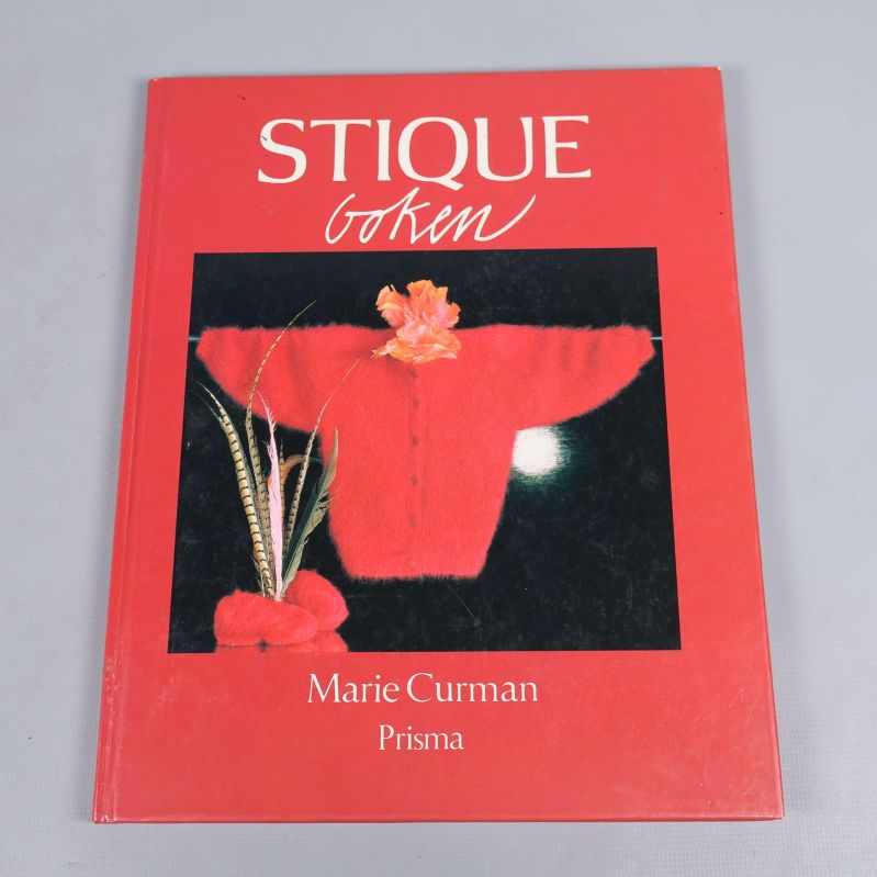 Framsidan av boken Stiqueboken med röd pärm och stickat plagg