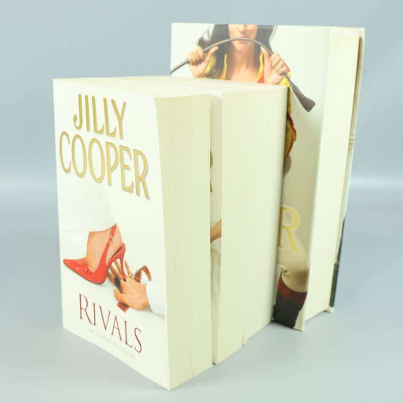 Öppen sida med tre stående Jilly Cooper böcker, boktjocklek synlig