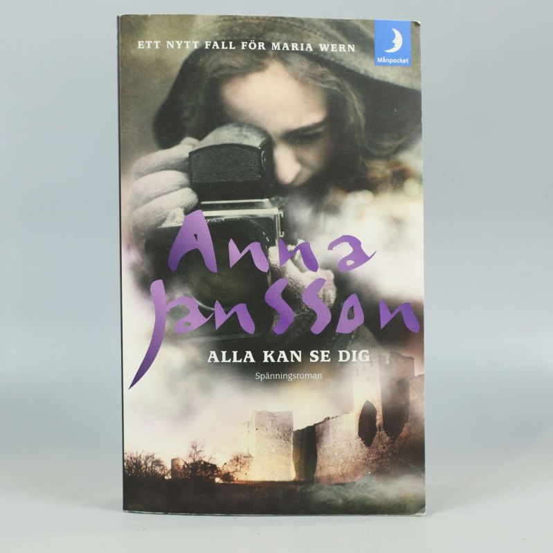 Framsida av pocketboken Alla kan se dig av Anna Jansson, med kvinna och kamera