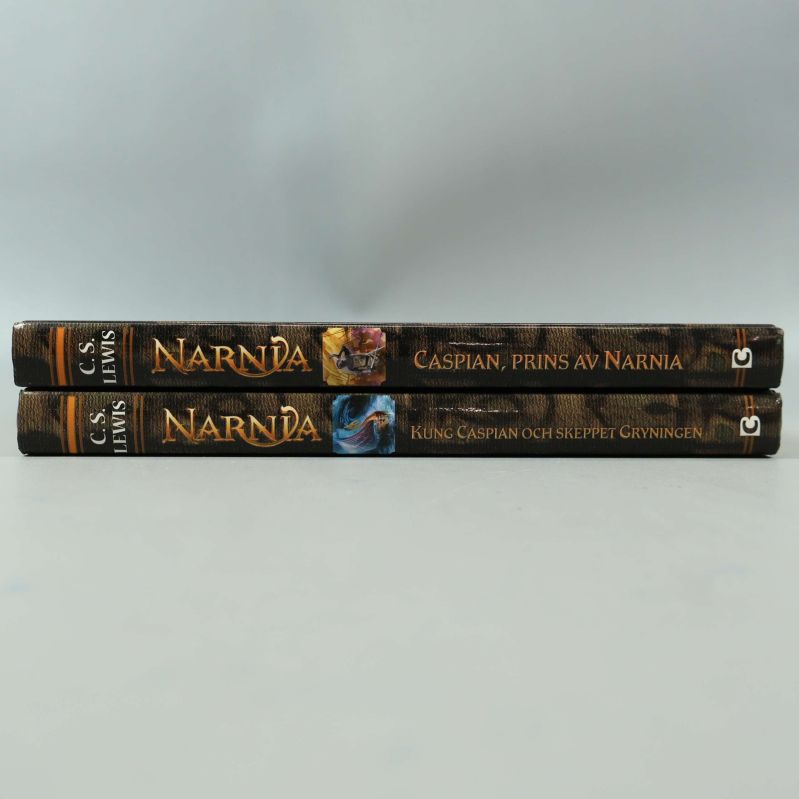 Ryggen på två Narnia-böcker med guldfärgade titlar och motiv
