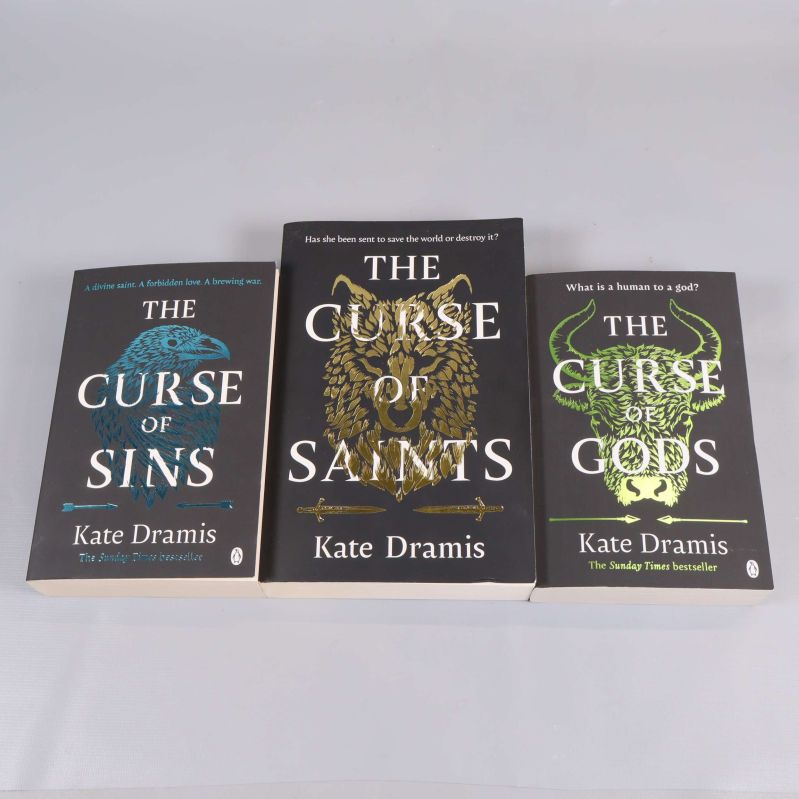 Tre böcker ur The Curse-serien av Kate Dramis med mörka omslag och guld, blå och gröna detaljer
