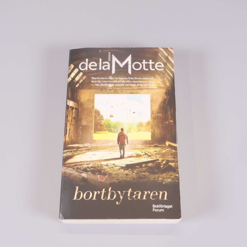 Framsidan av pocketboken Bortbytaren av Anders de la Motte med en person i ruiner