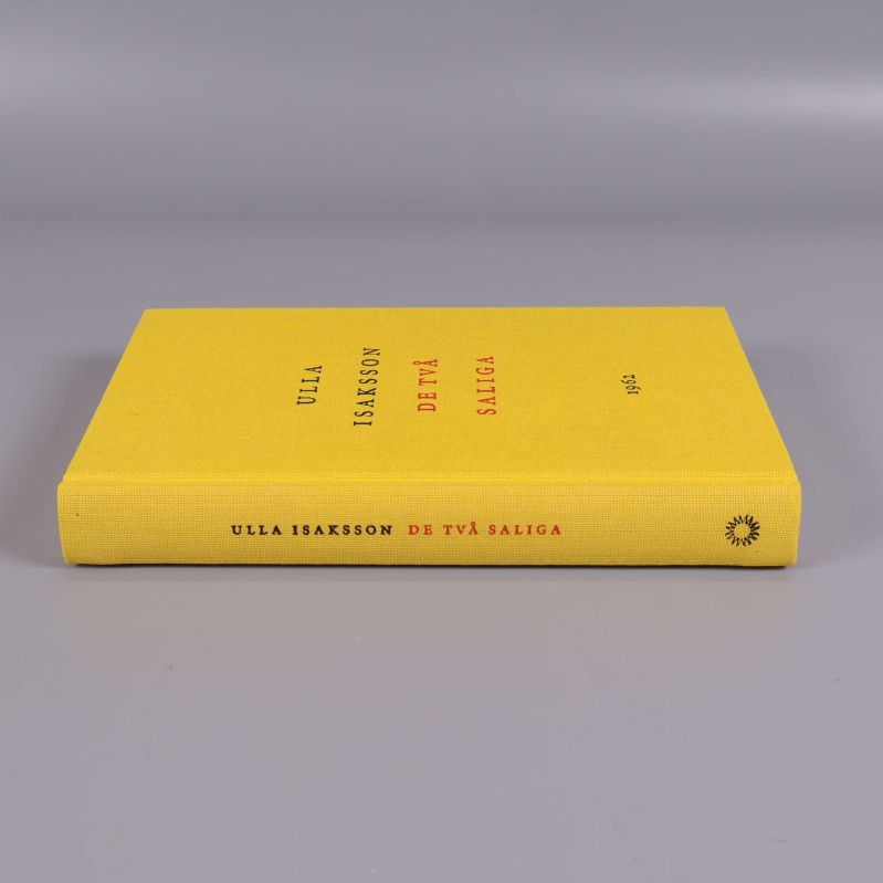 Boken De två saliga liggande, ryggen synlig med boktitel och författare