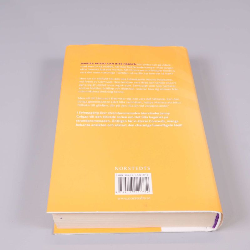 Baksida av boken Soluppgång över strandpromenaden med text och ISBN