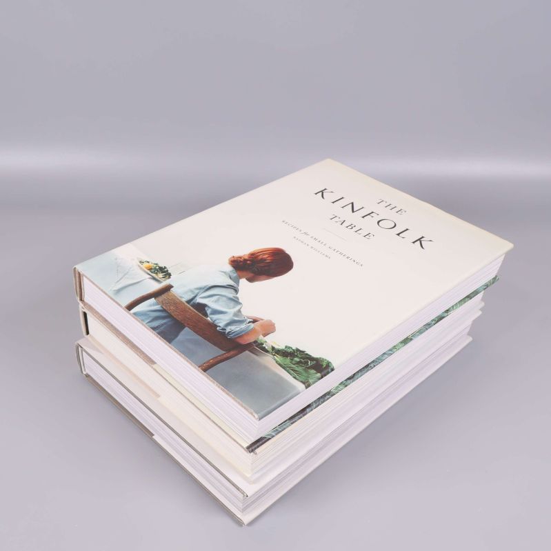 Uppslagen Kinfolk-bok med foto på man vid skrivbord, övriga Kinfolk-böcker i bakgrunden