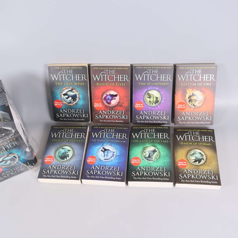 Alla åtta The Witcher böcker stående i två rader, framsidorna synliga i olika färger