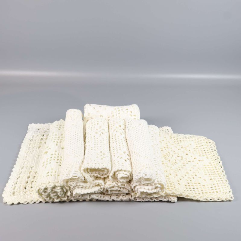 Flera hoprullade gräddvita virkade fyrkantiga dukar på rad