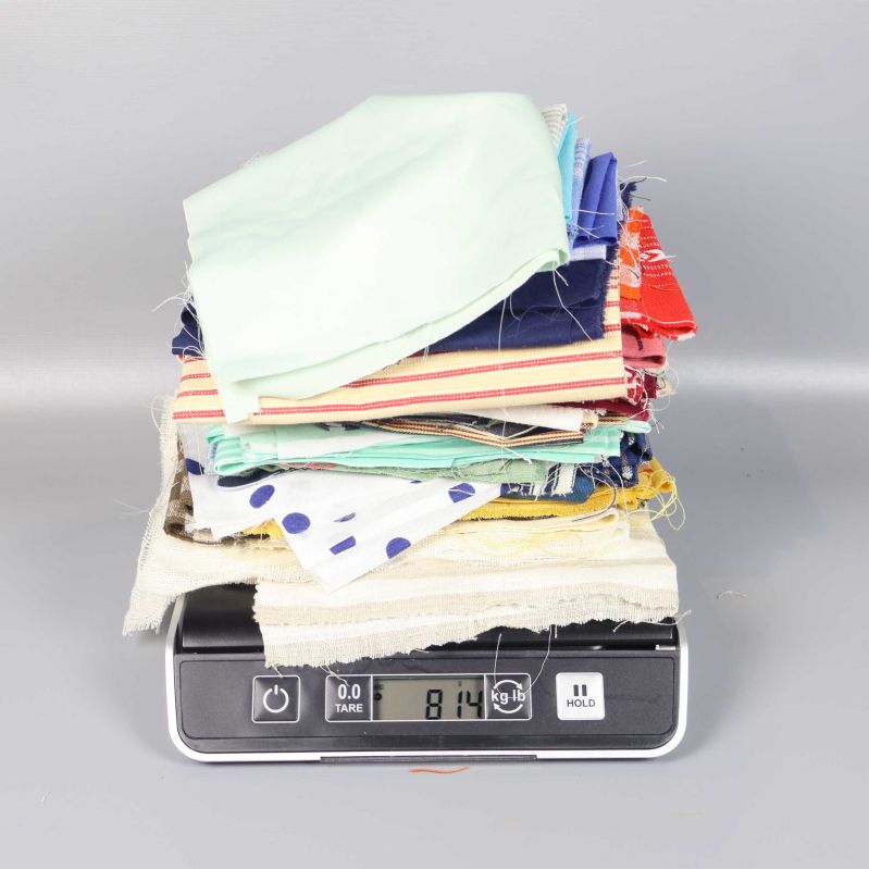 Tygbitar i blandade färger vägs på våg, visar 814 g