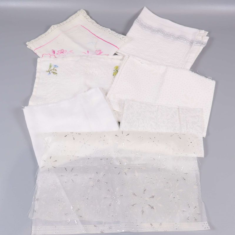 Närbild på vita och ljusa textilbitar med spets och brodyr