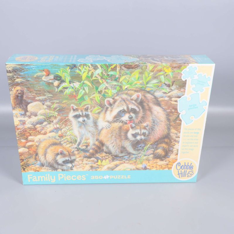 Framsidan av pussellåda med illustration på tvättbjörnsfamilj