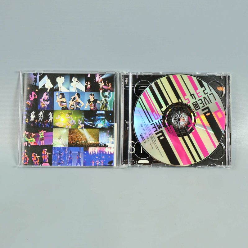 Öppen CD-fodral med Perfume livealbum och färgglad skiva samt fotocollage