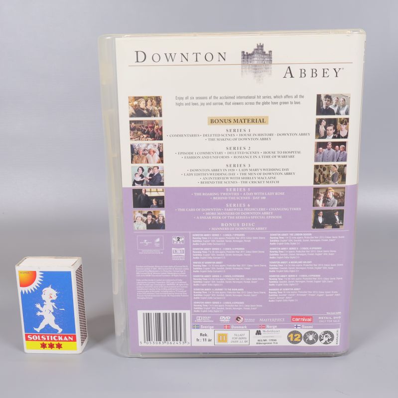 Baksidan av Downton Abbey DVD-box med beskrivning och matchask för storleksjämförelse