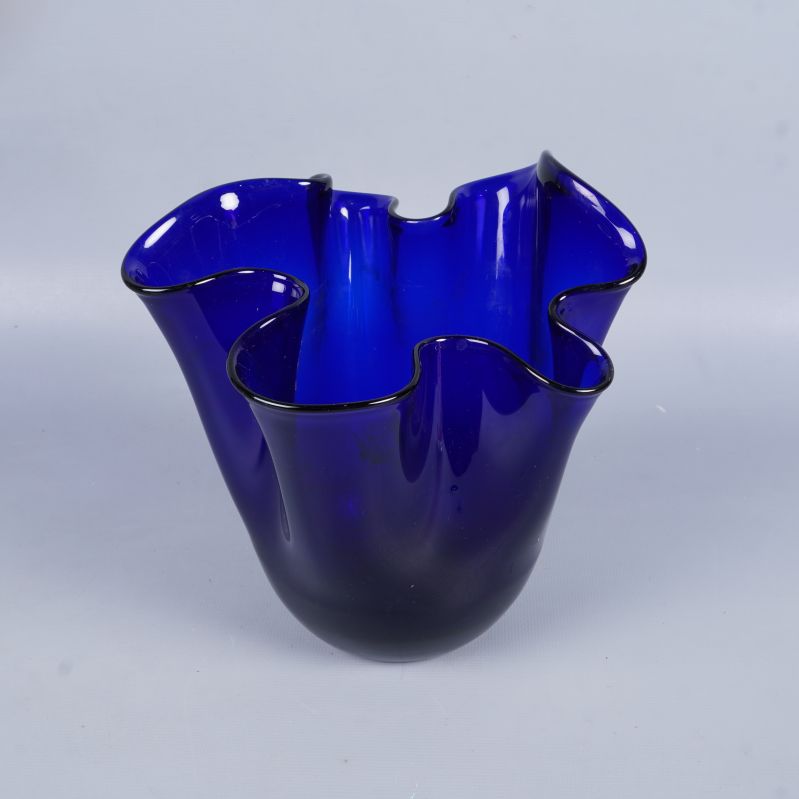 Vas i blått glas med vågig topp mot ljus bakgrund