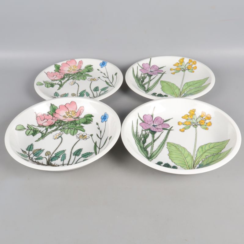 Fyra assietter med olika blommotiv på grå bakgrund