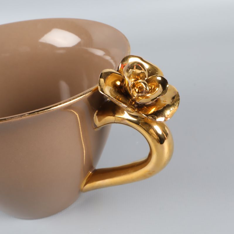 Närbild på guldfärgad blomma på koppens handtag