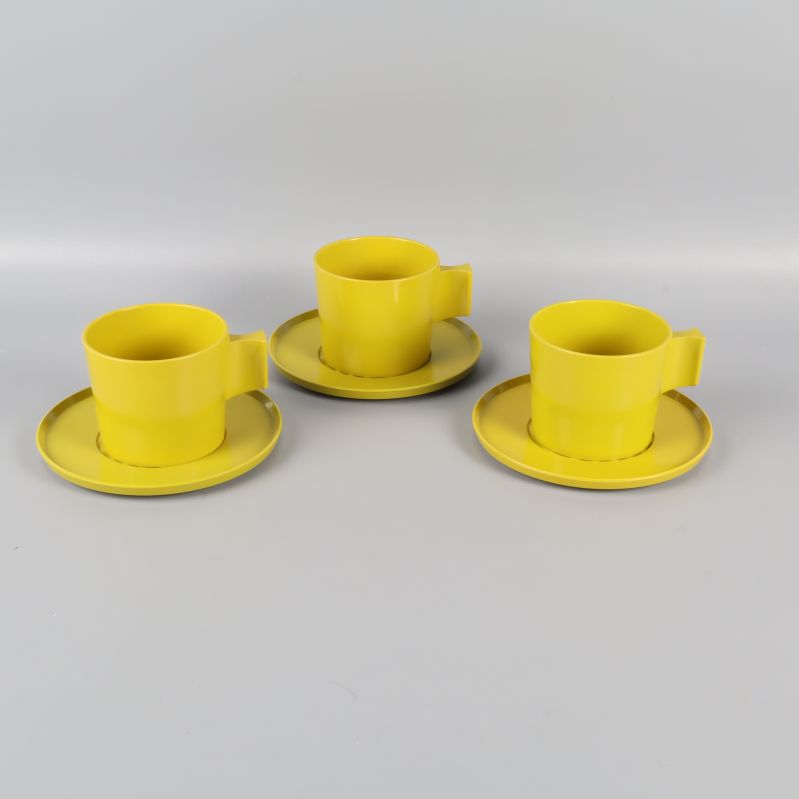 Tre gula/gröna koppar med tillhörande fat uppställda