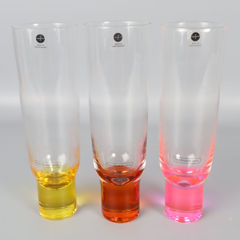 Tre champagneglas med gul, orange och rosa fot sida vid sida