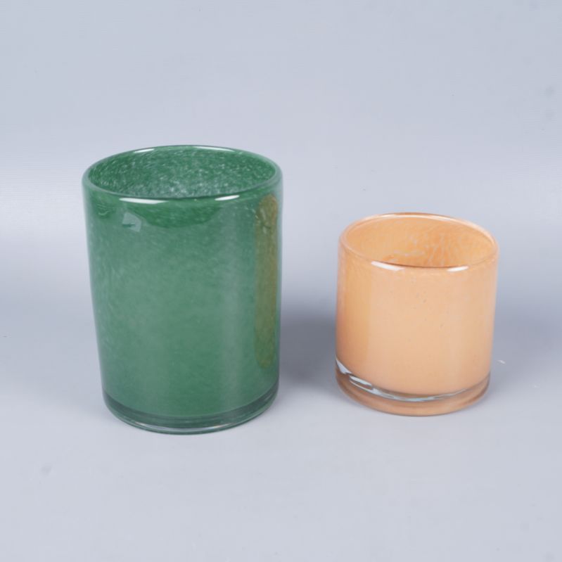 Två cylindriska ljuslyktor i grönt och aprikos