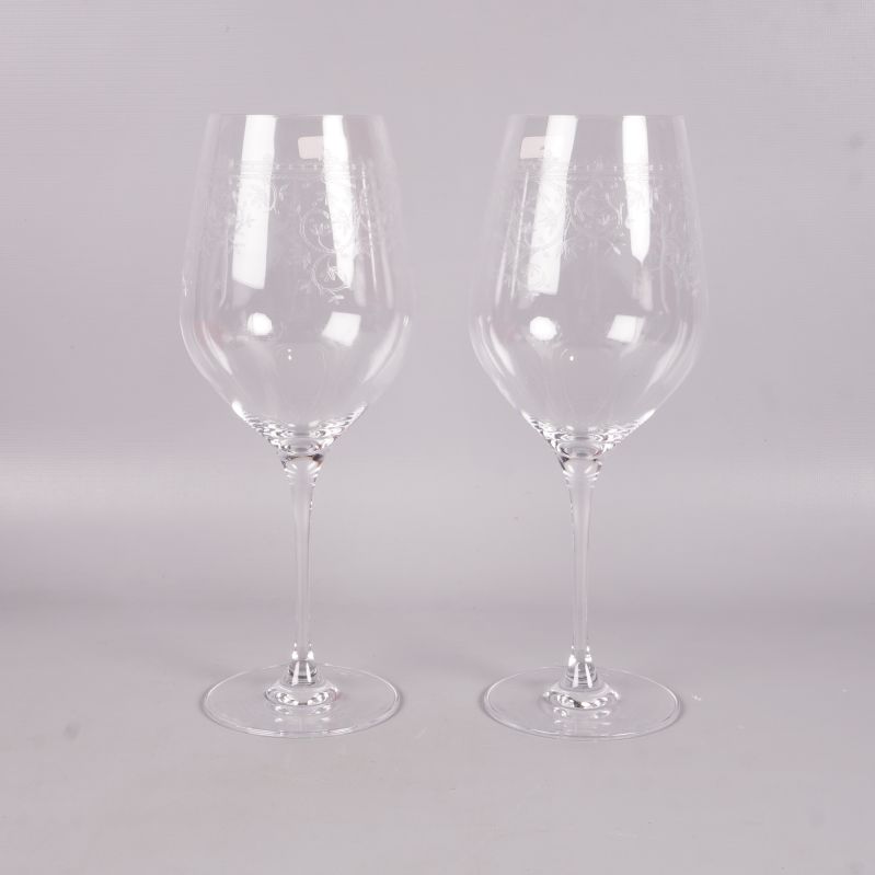 Framifrån två vinglas med tunn stjälk och graverat motiv