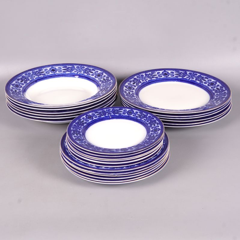 Flera tallrikar med blå mönstrad kant staplade på varandra på grå yta