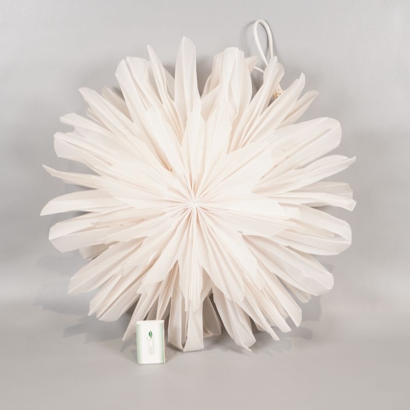 Stjärnformad pappersdekoration bredvid ett tändsticksfodral för storleksreferens