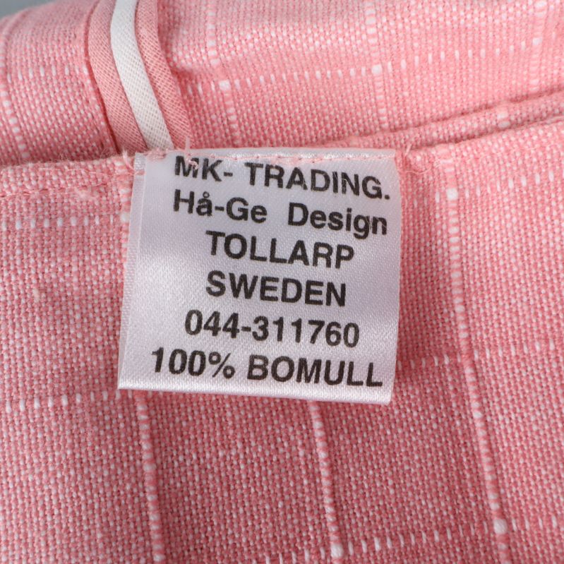 Textiletikett med information om MK-TRADING och 100% bomull