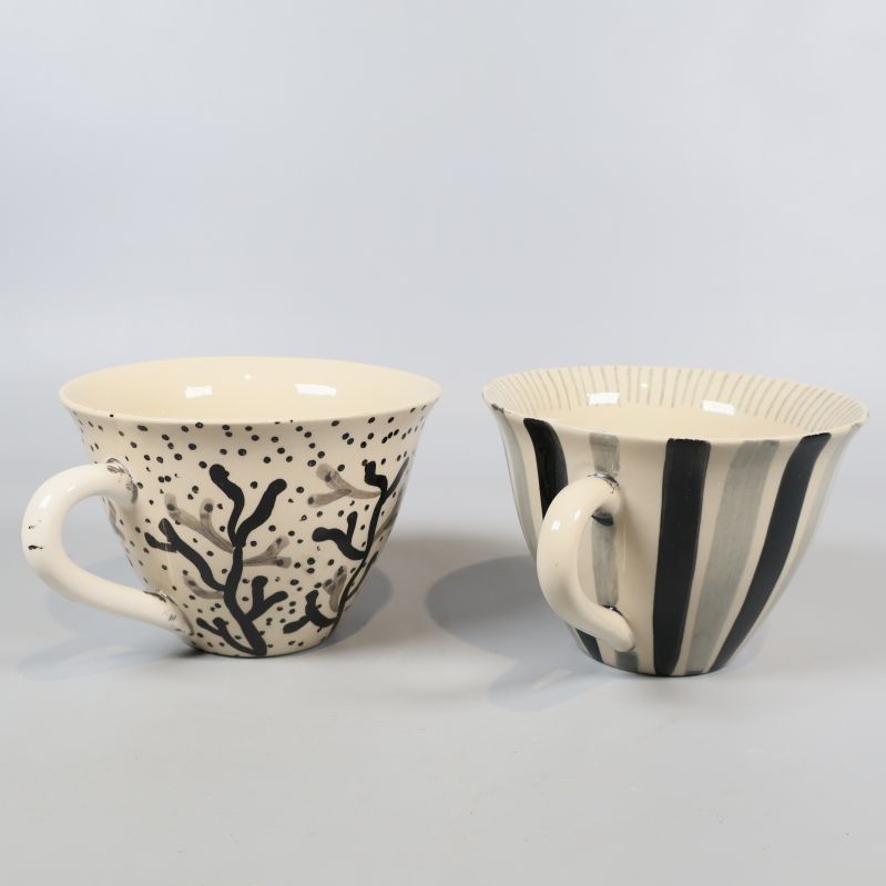 Två handmålade koppar med svartvita mönster sida vid sida
